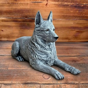 May include: A gray dog statue in a relaxed pose, with its front paws extended. The statue has detailed fur and facial features, including alert eyes and pointed ears. The dog is lying on a wooden surface with a wooden background.