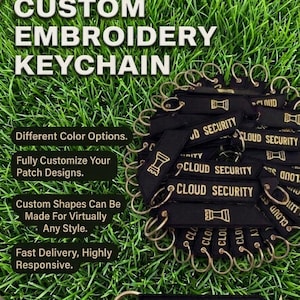 Puede incluir: Llaveros bordados negros con texto dorado "CLOUD SECURITY". Cada llavero tiene un anillo dorado y un gráfico dorado. La imagen también muestra el texto "CUSTOM EMBROIDERY KEYCHAIN". El fondo es hierba verde.