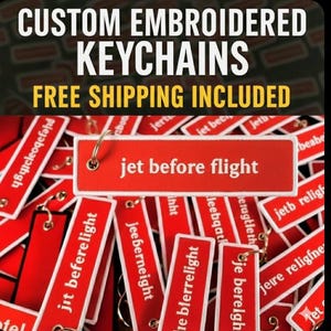 Könnte beinhalten: Rote rechteckige Schlüsselanhänger mit weißem Text, darunter "jet before flight" und andere Phrasen. Das Bild zeigt auch den Text "CUSTOM EMBROIDERED KEYCHAINS". Die Schlüsselanhänger haben Metallringe.