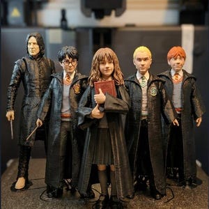 May include: A group of five detailed figurines from the Harry Potter series. The figures include Severus Snape, Harry Potter, Hermione Granger, Draco Malfoy, and Ron Weasley, all wearing their Hogwarts uniforms. The figures are standing in front of a 3D printer.