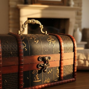 Op de afbeelding: Een decoratieve kist in antieke stijl met een donkere afwerking, goudkleurige hardware en afwerking. De kist heeft een handvat, een grendel en sierlijke details. De houten kist heeft een geweven patroon op de zijkanten en is afgewerkt met donkerbruin hout.