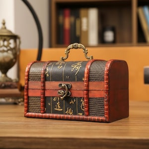 Op de afbeelding: Een kleine houten kist in antieke stijl met een donkerbruine afwerking, rode randen en een decoratieve metalen sluiting. De kist heeft een handvat en is versierd met goudkleurige Chinese karakters.