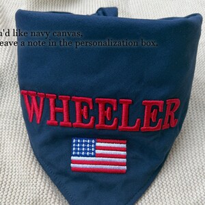 May include: A navy blue triangular pet bandana featuring the embroidered red text WHEELER and a small embroidered American flag. The fabric includes the printed text: If you'd like navy canvas, just leave a note in the personalisation box.