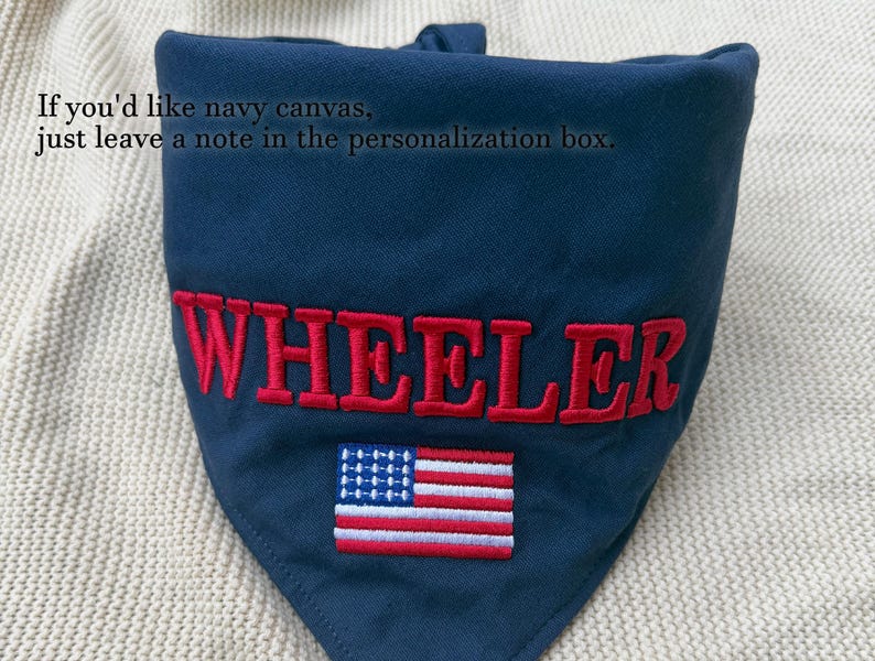 May include: A navy blue triangular pet bandana featuring the embroidered red text WHEELER and a small embroidered American flag. The fabric includes the printed text: If you'd like navy canvas, just leave a note in the personalisation box.