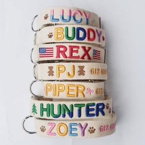 May include: A stack of six beige fabric pet collars featuring embroidered names and icons. The names include LUCY, BUDDY, REX, PJ, PIPER, HUNTER, and ZOEY. Each collar has a metal D-ring and displays colourful thread designs like paw prints, flags, bears, and trees.