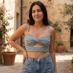 Può includere: Top corto all'uncinetto blu chiaro e bianco con design a chiave. Il top ha spalline sottili e un motivo a scacchi. La modella indossa jeans blu.
