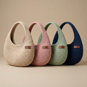 May include: Four crochet shoulder bags in beige, pink, green, and navy blue. Each bag has a rounded shape, a thick handle, and a small brown leather tag. The bags are made of a textured, chunky yarn.