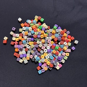 May include: A collection of colorful dice scattered on a dark surface. The dice are various colors, including red, green, purple, and yellow, with white pips. The dice are of different sizes and shapes, creating a visually interesting assortment.