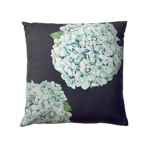 Puede incluir: Cojín decorativo cuadrado con fondo gris oscuro. El cojín presenta dos grandes ilustraciones detalladas de flores de hortensia azules y blancas con hojas verdes. El diseño floral está centrado en el cojín.