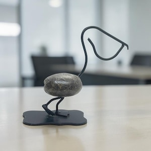 以下が含まれることがあります： 滑らかな灰色の川石を胴体とし、黒い金属ワイヤーで首、頭、くちばしを形作った鳥の装飾彫刻。鳥は平らな黒い4つ葉型の金属ベースの上に立っており、バランスの取れた安定した構造を作り出しています。