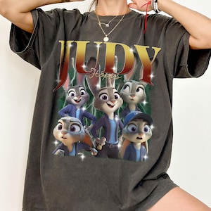 May include: Dark gray t-shirt featuring a graphic of Judy Hopps and other characters from the animated movie Zootopia. The word "JUDY" is in gold lettering, with "Hopps" below. The shirt has a vintage, distressed look.