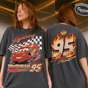 May include: Dark gray t-shirt featuring Lightning McQueen from the Cars movie. The front graphic shows the car with a checkered flag and the text "Lightning McQueen 95". The back displays "95" in flames and "Lightning McQueen".