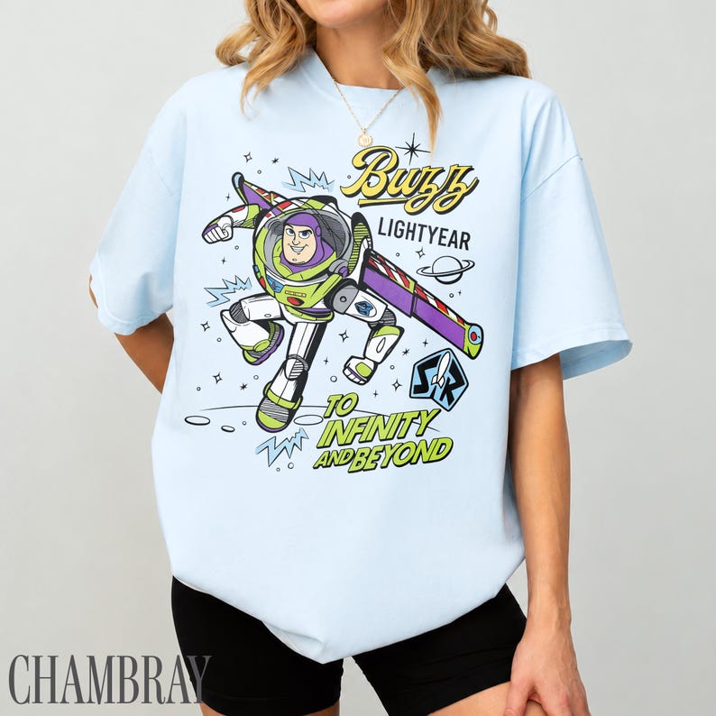 Pode incluir: T-shirt azul claro com um desenho de Buzz Lightyear. O design inclui o texto "Buzz Lightyear" e "To Infinity and Beyond". O desenho &eacute; em estilo cartoon. A t-shirt &eacute; de cor azul claro.