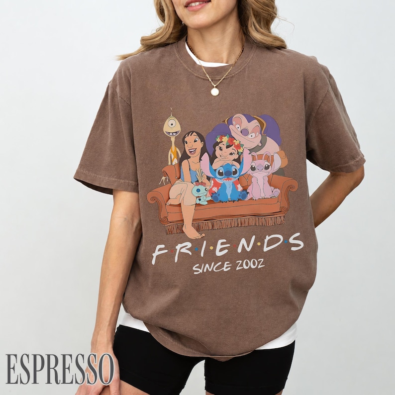 May include: Brown t-shirt with a graphic of Lilo & Stitch characters on a brown sofa. The word "FRIENDS" is printed below the sofa, with "SINCE 2002" underneath. The shirt has a relaxed fit. The word "ESPRESSO" is printed at the bottom left.