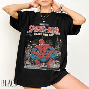 May include: Black t-shirt featuring a Marvel Studios Spider-Man graphic. The design includes the words "Spider-Man Brand New Day" and an illustration of Spider-Man crouching in front of a cityscape. The word "BLACK" is printed at the bottom.