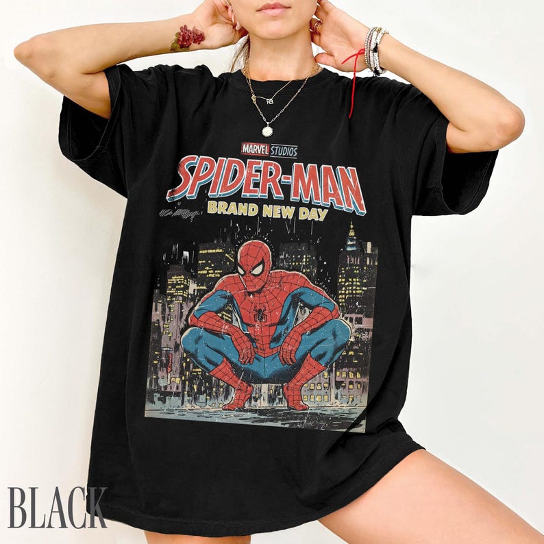 May include: Black t-shirt featuring a Marvel Studios Spider-Man graphic. The design includes the words "Spider-Man Brand New Day" and an illustration of Spider-Man crouching in front of a cityscape. The word "BLACK" is printed at the bottom.