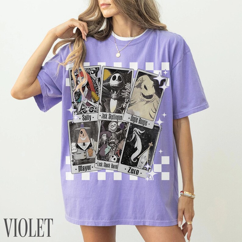 May include: Violet-colored t-shirt featuring character cards from The Nightmare Before Christmas. The cards include Sally, Jack Skellington, Oogie Boogie, Mayor, Lock Shock Barrel, and Zero. The shirt has a white checkered pattern.