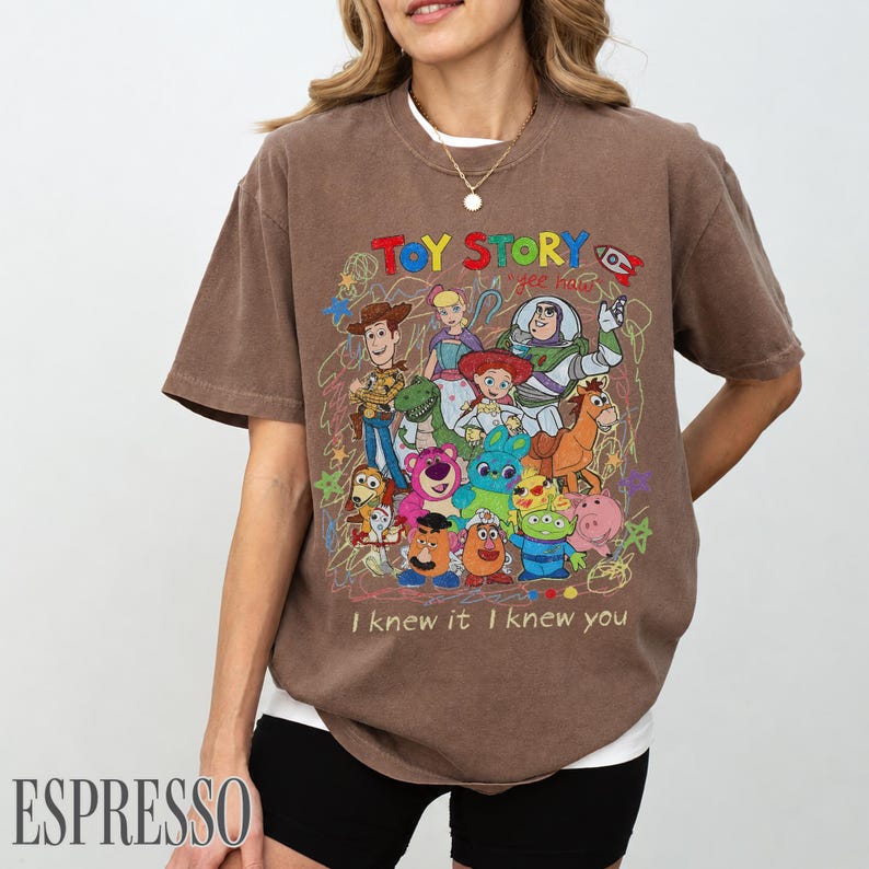 May include: A brown short-sleeve t-shirt featuring a colourful graphic print of Toy Story characters including Woody, Buzz Lightyear, and Jessie. The design includes the text "TOY STORY" and "I knew it I knew you" with scribbled line art accents.