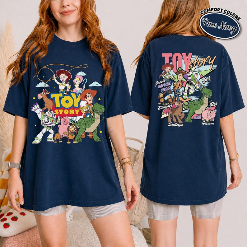 K&ouml;nnte beinhalten: Marineblaues T-Shirt mit einem farbenfrohen Design von Toy Story-Charakteren, darunter Woody, Buzz Lightyear und Rex. Auf der Vorderseite des Shirts befindet sich das Toy Story-Logo. Auf der R&uuml;ckseite des Shirts steht "Toy Story" und die Charaktere. Hergestellt von Comfort Colors.