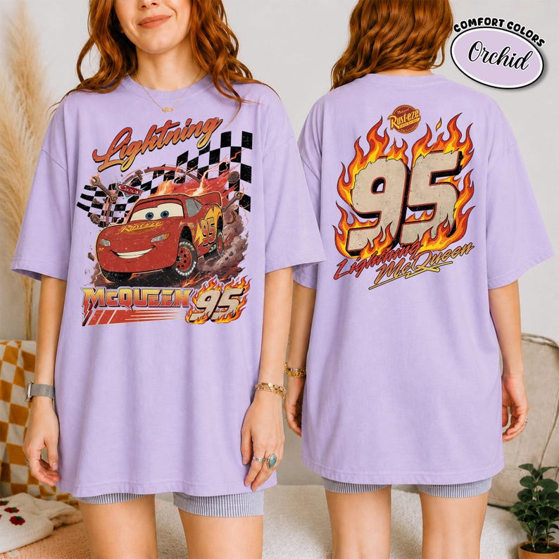 May include: Lavender t-shirt featuring Lightning McQueen from the movie Cars. The front graphic shows McQueen racing with the text "Lightning McQueen 95". The back of the shirt has "95" in flames and "Lightning McQueen" text.