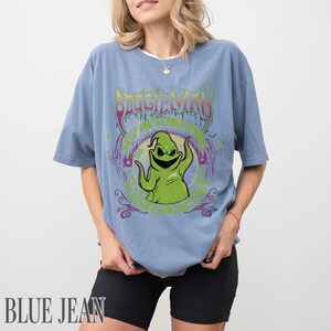 May include: A light blue t-shirt with a graphic of Oogie Boogie from The Nightmare Before Christmas. The design includes the text "BOOGIEMAN" in a purple, stylized font, and the text "ANYTHING BUT LIVE" in green.