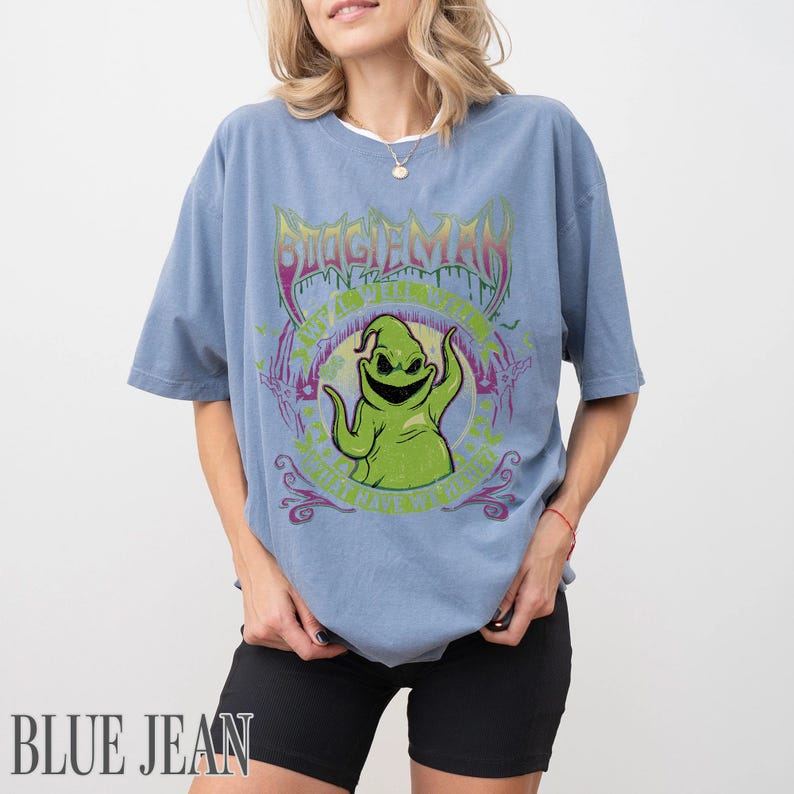May include: A light blue t-shirt with a graphic of Oogie Boogie from The Nightmare Before Christmas. The design includes the text "BOOGIEMAN" in a purple, stylized font, and the text "ANYTHING BUT LIVE" in green.