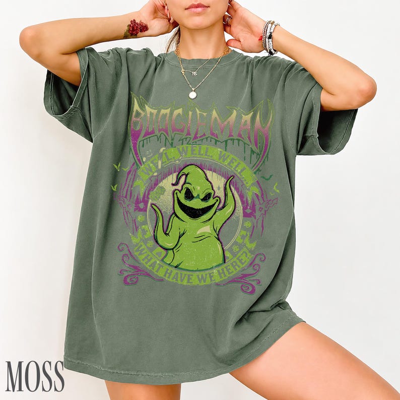 May include: Moss green t-shirt with a graphic of Oogie Boogie from The Nightmare Before Christmas. The design includes the text "BOOGIE MAN" and "WELL WELL WELL... WHAT HAVE WE HERE?" in purple and green.