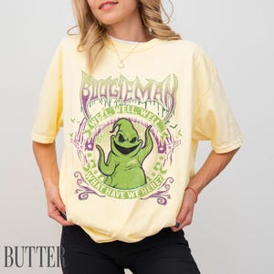 May include: Pale yellow t-shirt with a graphic of Oogie Boogie from The Nightmare Before Christmas. The design includes the text "Oogie Boogie" and "We'll, Well, Well... What Have We Here?" in green and purple.