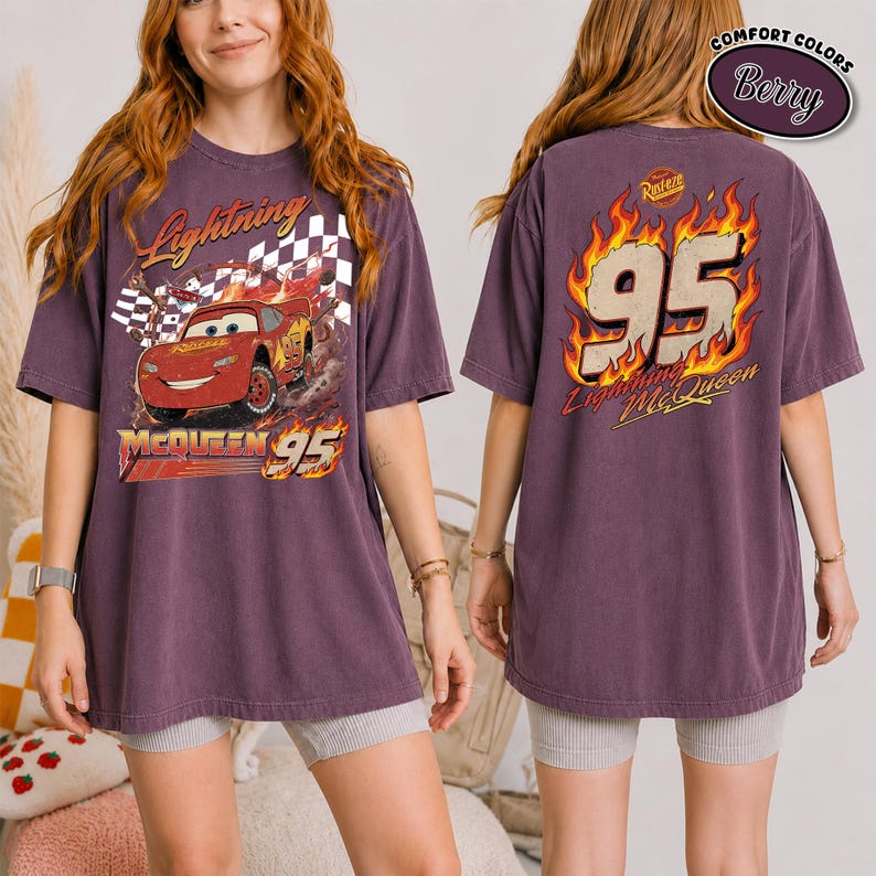 May include: Berry-colored t-shirt featuring Lightning McQueen from the Cars movie. The front graphic shows McQueen racing with the text "Lightning McQueen" and "95." The back displays "95" in flames with "Lightning McQueen" below. The shirt has a vintage look.