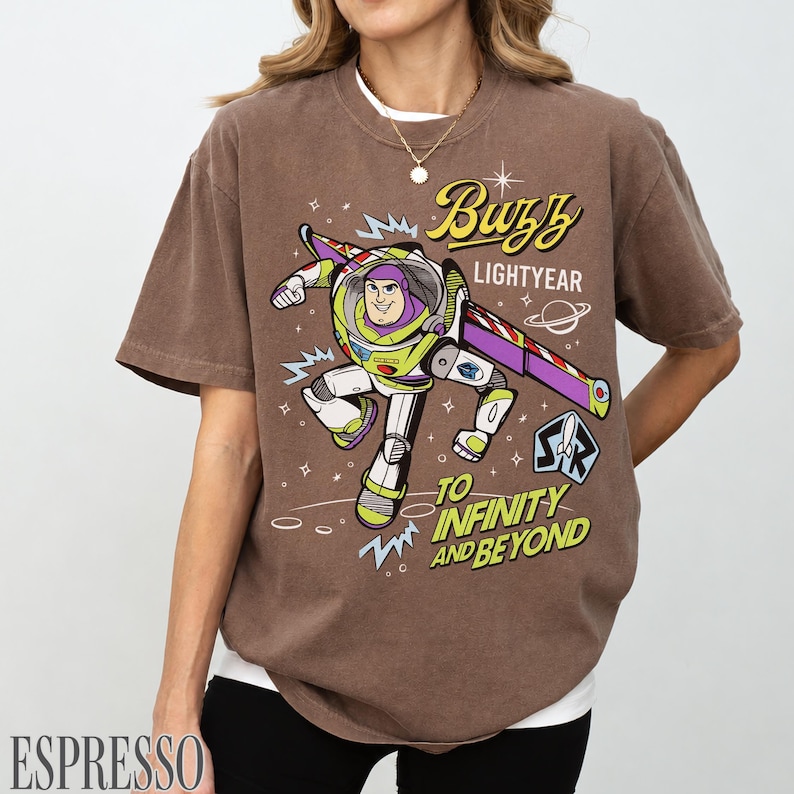 Pode incluir: Camiseta marrom com um desenho do Buzz Lightyear. O design inclui o texto "Buzz Lightyear" e "To Infinity and Beyond". A camiseta tem um visual vintage e desgastado.