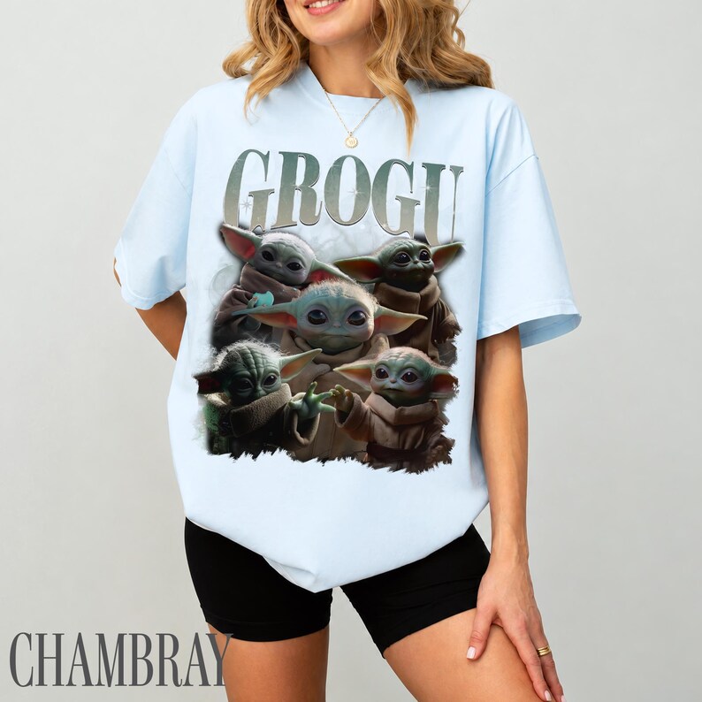 K&ouml;nnte beinhalten: Hellblaues T-Shirt mit dem Wort "GROGU" in Silber &uuml;ber einer Grafik von Grogu, auch bekannt als Baby Yoda, aus Star Wars. Die Grafik zeigt Grogu in verschiedenen Posen. Das Shirt ist aus einem weichen Material.