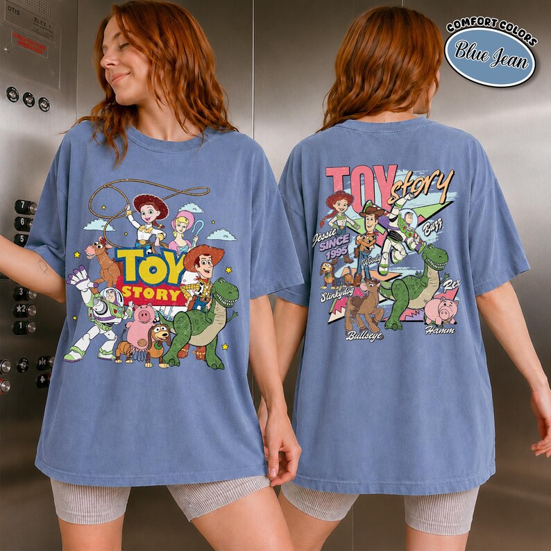 K&ouml;nnte beinhalten: Blaues Jeans-T-Shirt mit einem farbenfrohen Toy Story-Motiv, darunter Woody, Buzz Lightyear und Rex. Auf der Vorderseite befindet sich das Toy Story-Logo. Die R&uuml;ckseite zeigt das Toy Story-Logo und weitere Charaktere.