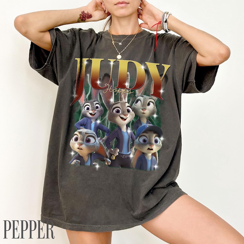 May include: Dark gray t-shirt featuring a graphic of Judy Hopps and other characters from the animated movie Zootopia. The word "JUDY" is in gold lettering, with "Hopps" below. The shirt has a vintage, distressed look.