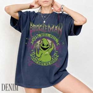 May include: Navy blue t-shirt with a graphic of Oogie Boogie from The Nightmare Before Christmas. The design includes the text "BOOGIEMAN" and "WELL, WELL, WELL... WHAT HAVE WE HERE?" in a circular design.