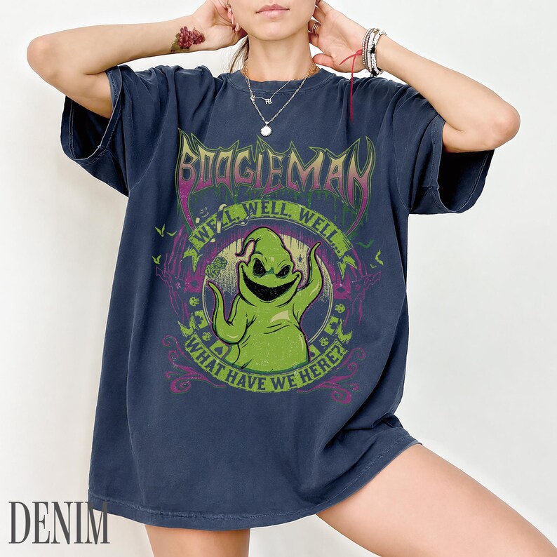 May include: Navy blue t-shirt with a graphic of Oogie Boogie from The Nightmare Before Christmas. The design includes the text "BOOGIEMAN" and "WELL, WELL, WELL... WHAT HAVE WE HERE?" in a circular design.