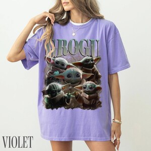 K&ouml;nnte beinhalten: Violettes T-Shirt mit einer Grafik von Grogu aus The Mandalorian. Das Design zeigt mehrere Bilder von Grogu in verschiedenen Posen. Das Wort "GROGU" ist oben in einer Farbverlaufs-Schriftart aufgedruckt. Das Wort "VIOLET" ist unten aufgedruckt.