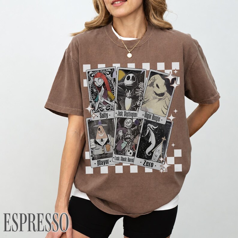 May include: Espresso-colored t-shirt featuring six character cards from The Nightmare Before Christmas. The cards include Sally, Jack Skellington, Oogie Boogie, Mayor, Lock Shock Barrel, and Zero. The shirt has a crew neck and short sleeves.
