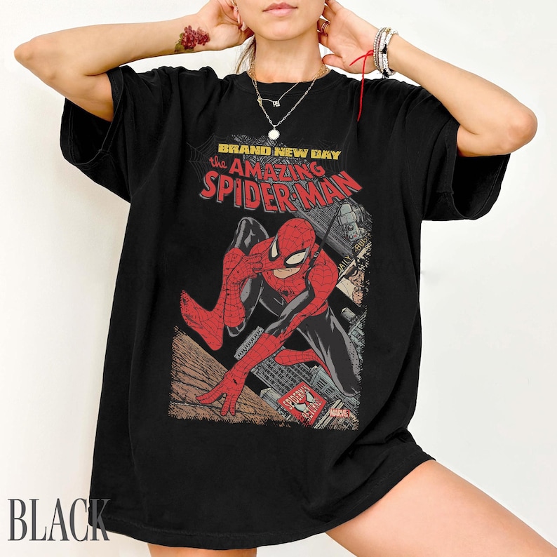May include: Black t-shirt featuring a vintage comic book graphic of Spider-Man. The design includes the text "BRAND NEW DAY the AMAZING SPIDER-MAN" in red and white. The shirt is a classic crew neck style.