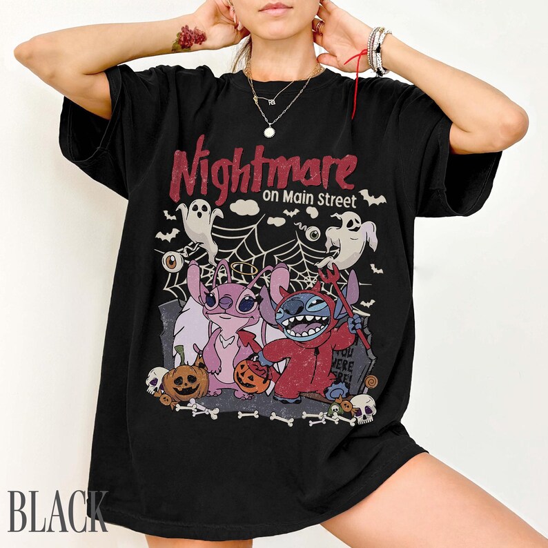May include: A black short-sleeve t-shirt featuring a graphic print with the text Nightmare on Main Street. The design includes two cartoon characters, one pink and one blue, surrounded by ghosts, a spider web, pumpkins, and skulls.