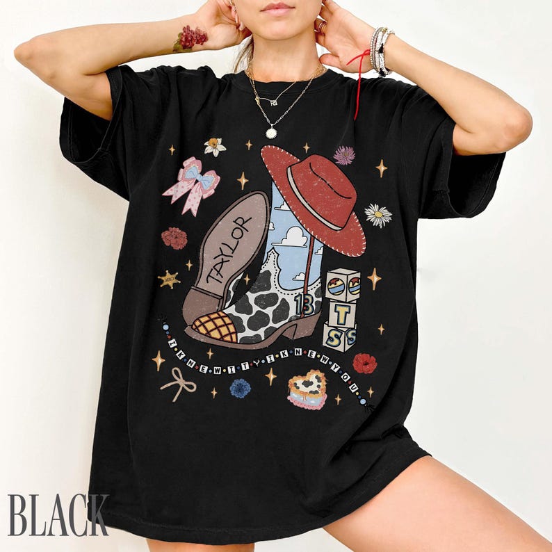 May include: A black t-shirt featuring a graphic print of a cow-print cowboy boot with the name Taylor, a red cowboy hat, building blocks with the letters T S, a pink bow, and small flowers. The text I KNEW YOU WERE TROUBLE is printed in a circular pattern.