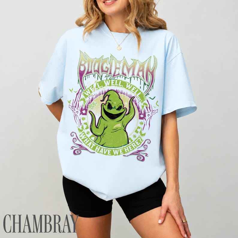 May include: Pale blue t-shirt with a green Oogie Boogie graphic. The design includes the text "BOOGIE MAN" above the character, with "WELL WELL WELL" and "WHAT HAVE WE HERE?" around it. A casual wear item.