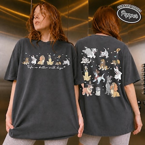 Puede incluir: Camiseta gris oscuro Comfort Colors con ilustraciones de perros de dibujos animados. La parte delantera muestra la frase "life is better with dogs". La parte trasera de la camiseta tiene m&aacute;s ilustraciones de perros. La camiseta tiene un corte relajado.