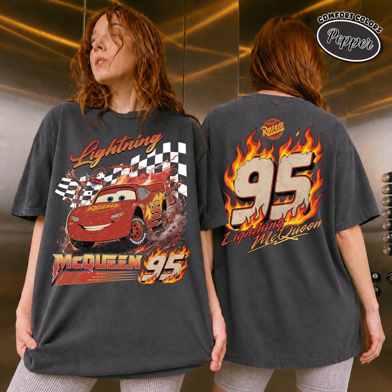 May include: Dark gray t-shirt featuring Lightning McQueen from the Cars movie. The front graphic shows the car with a checkered flag and the text "Lightning McQueen 95". The back displays "95" in flames and "Lightning McQueen".