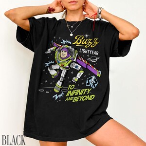 Pode incluir: Camiseta preta com um gr&aacute;fico de Buzz Lightyear em pose de voo, com as palavras "Buzz Lightyear" e "To Infinity and Beyond". O design inclui um tema espacial com estrelas e planetas.