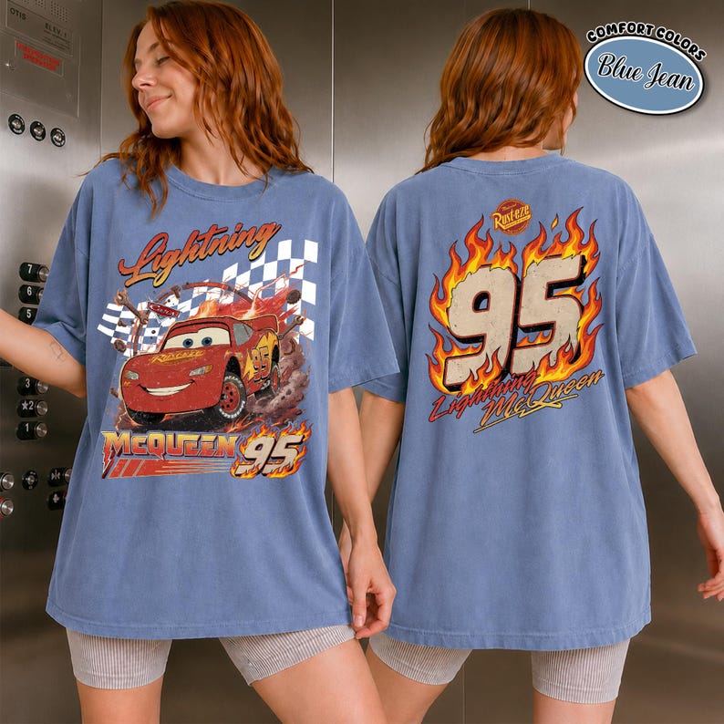 May include: Blue jean-colored t-shirt featuring Lightning McQueen from the movie Cars. The front graphic shows the car racing with the text "Lightning McQueen" and "95". The back of the shirt has the number "95" in flames and the text "Lightning McQueen".