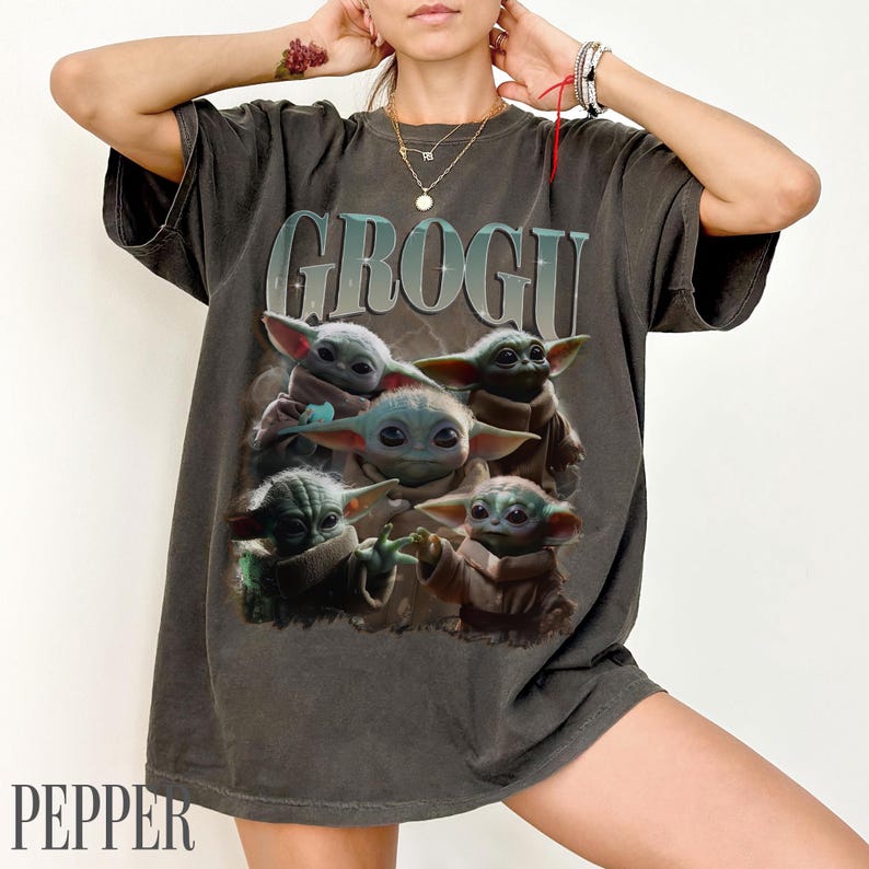 K&ouml;nnte beinhalten: Dunkelgraues T-Shirt mit dem Wort "GROGU" &uuml;ber einer Grafik von f&uuml;nf Grogu-Charakteren. Die Grogu-Charaktere sind hellgr&uuml;n mit gro&szlig;en Ohren. Das T-Shirt hat ein Vintage-Aussehen. Das Wort "PEPPER" ist unten aufgedruckt.