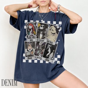 May include: Navy blue t-shirt featuring character cards from The Nightmare Before Christmas. The cards include Sally, Jack Skellington, Oogie Boogie, Mayor, Lock Shock Barrel, and Zero. The word "DENIM" is printed at the bottom.