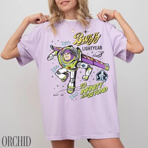 Pode incluir: Uma t-shirt lil&aacute;s com um desenho do Buzz Lightyear. O design inclui o texto "Buzz Lightyear" e "To Infinity and Beyond". A t-shirt tem mangas curtas e gola redonda.