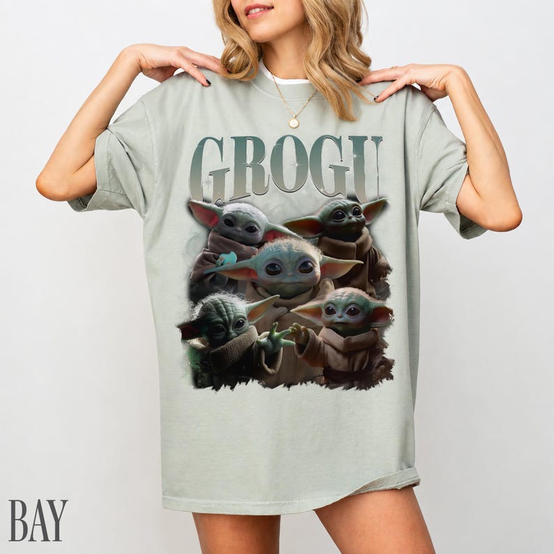 K&ouml;nnte beinhalten: Hellgr&uuml;nes T-Shirt mit dem Wort "GROGU" &uuml;ber einer Grafik von Grogu, der Figur aus Star Wars. Die Grafik zeigt Grogu in verschiedenen Posen. Das T-Shirt hat eine lockere Passform.
