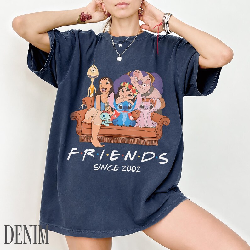 May include: Dark blue t-shirt with a cartoon graphic of characters from Lilo & Stitch on a brown sofa. The word "FRIENDS" is above "SINCE 2002" in white text. The word "DENIM" is printed in the bottom left corner of the t-shirt.